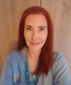 Dr Mcaree standing in front of a wooden door wearing a blue scrub top